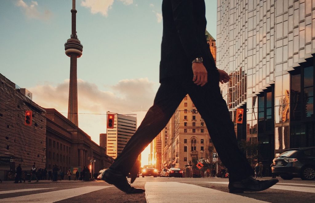 Shilouette of a man walking on the street with the CN tower in the background in Toronto