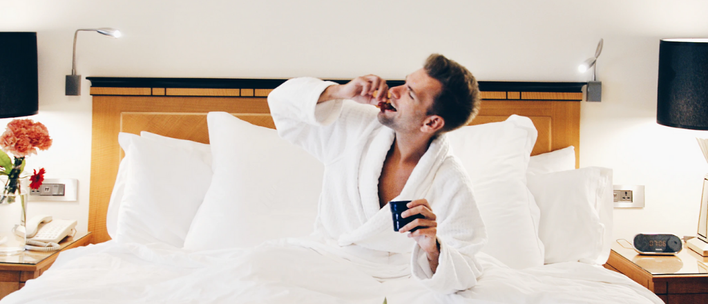 Man eats breakfast in bed of a luxury hotel suite